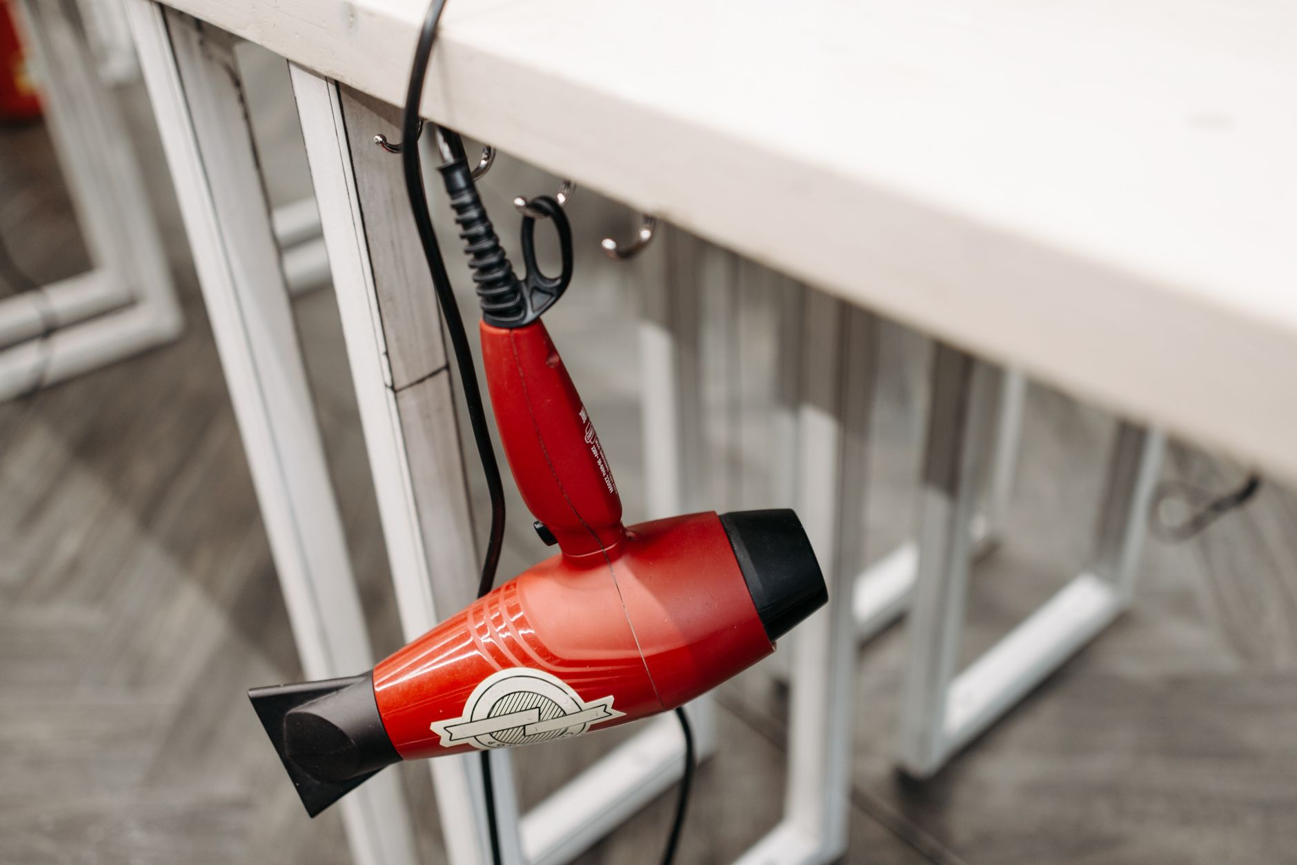 Close-up of a red hair dryer hanging from a white table indoors, showcasing product details.