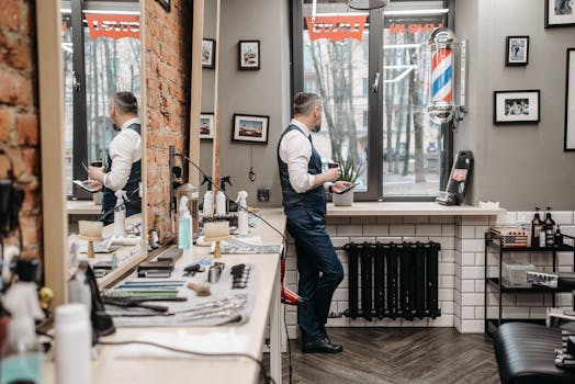 A well-dressed man standing in a modern barber shop, looking out the window.