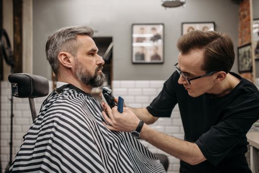 A professional barber precisely trimming a client's beard in a modern barbershop.