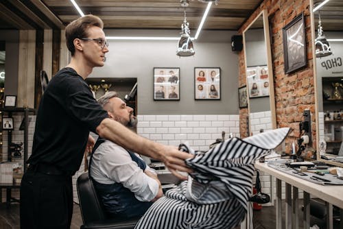A Barber Placing a Cape on a Client