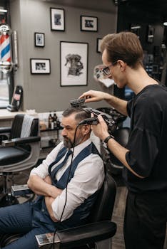 Barber using a hairbrush and clippers to style man's hair in a trendy barbershop.