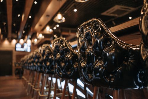 Free Elegant row of leather bar stools in a softly lit, upscale bar setting, ideal for a cozy atmosphere. Stock Photo
