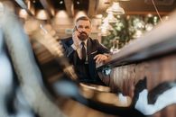 Bearded businessman in a suit having a phone conversation in a modern bar setting, with a warm ambiance.