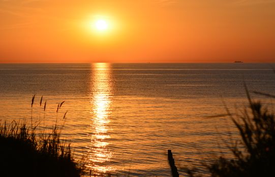 A breathtaking sunset over a tranquil ocean, reflecting warm orange hues across the water.