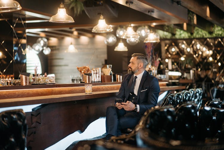 Man Holding A Smartphone Sitting At The Bar Counter