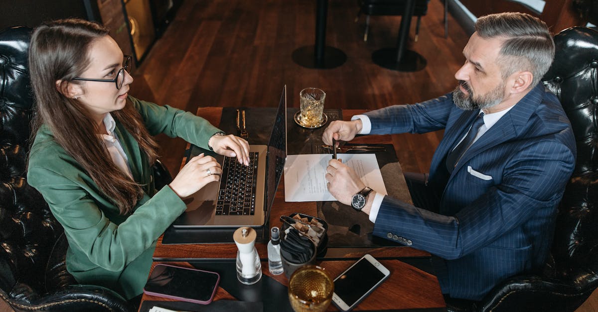 A businessman and businesswoman discuss documents over drinks in a stylish restaurant.