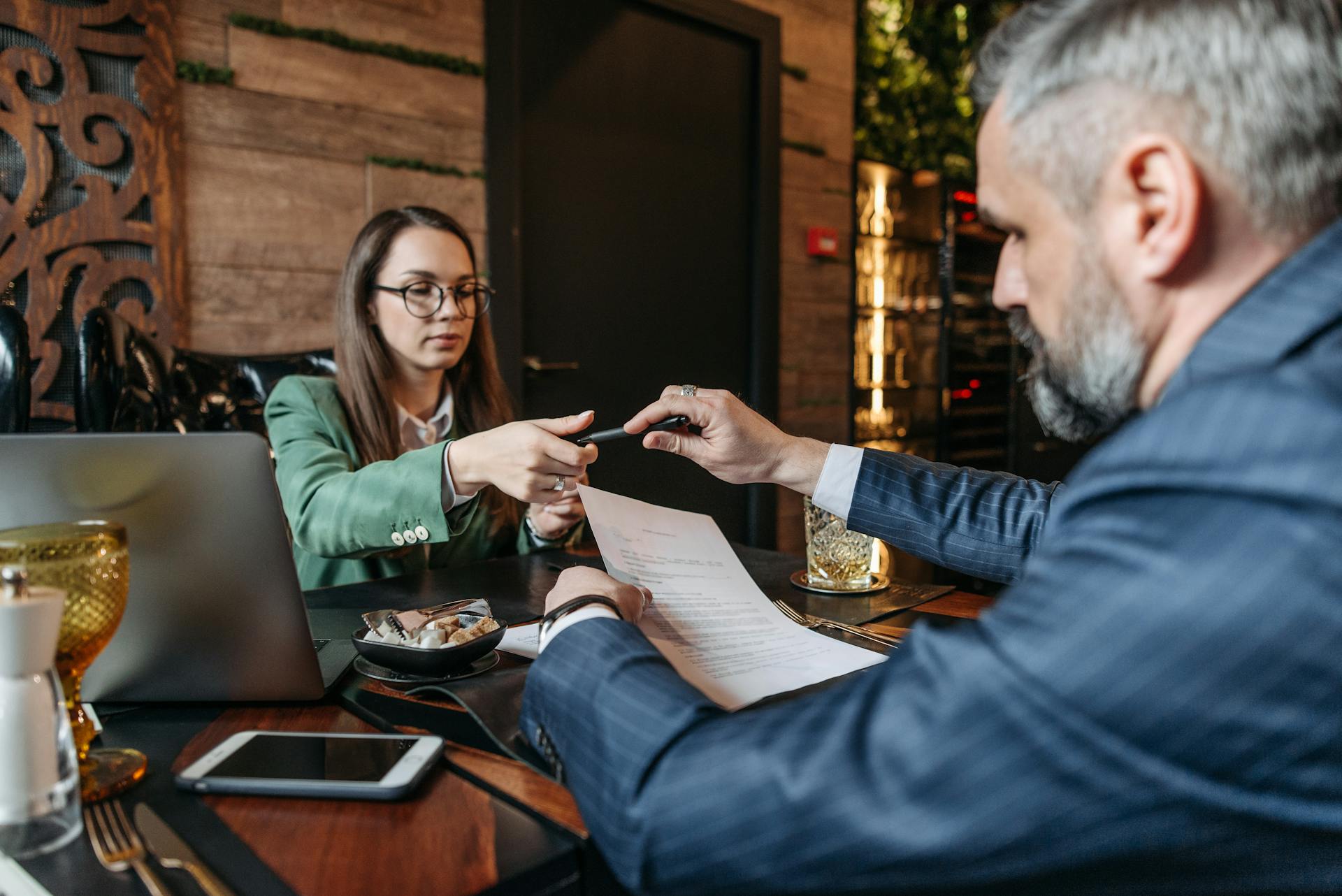 A man and woman review and sign a business contract in a stylish café setting.