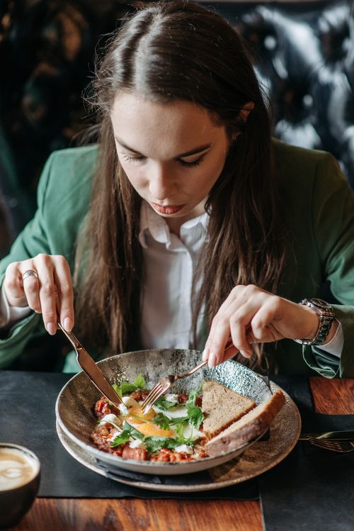 Free Young woman in green blazer dining on a healthy breakfast with bread and greens. Stock Photo