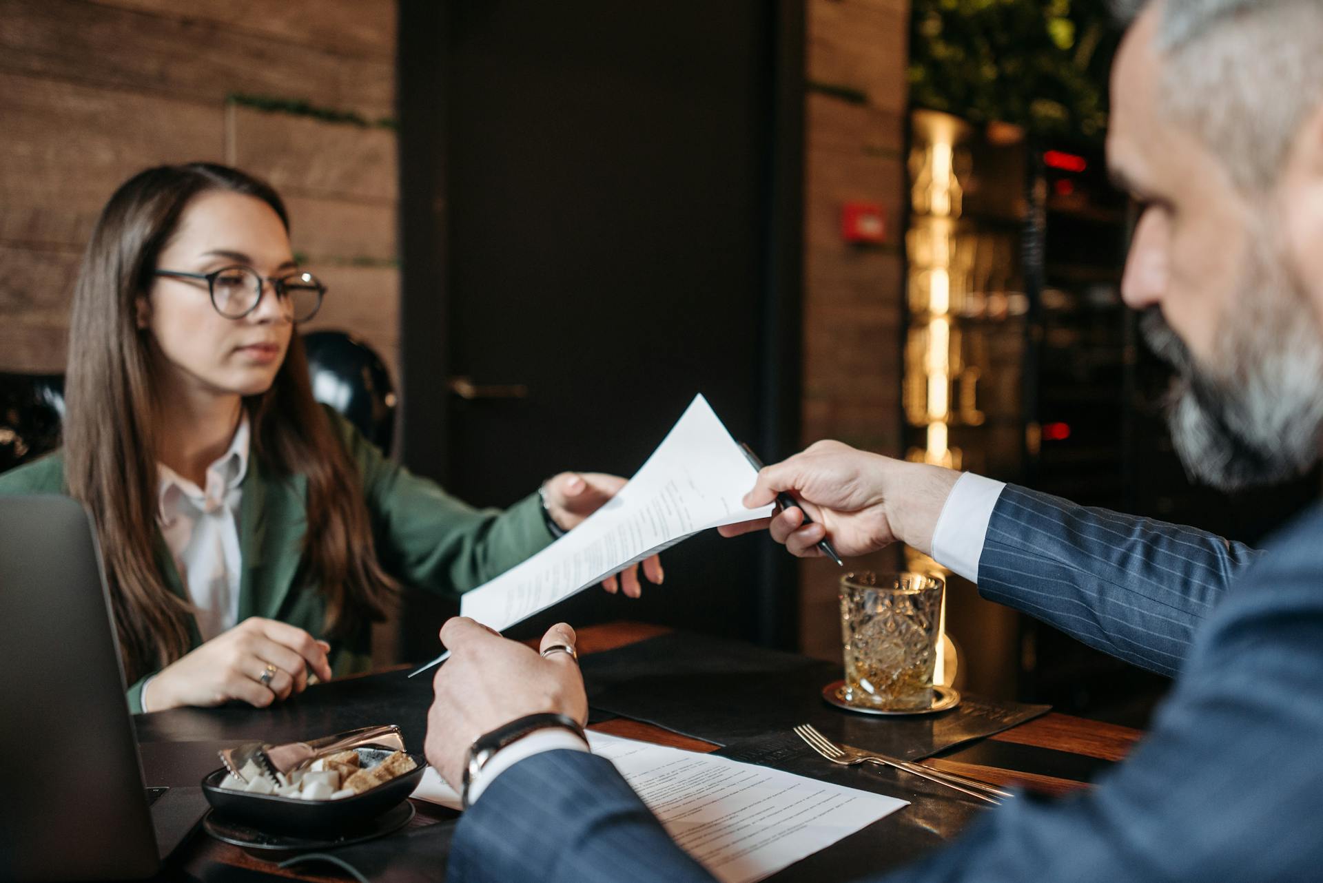 A man and woman exchanging documents during a professional meeting at an office table.