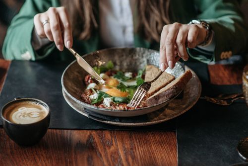 Free A person enjoys a breakfast dish with coffee in a cozy setting, emphasizing food artistry. Stock Photo