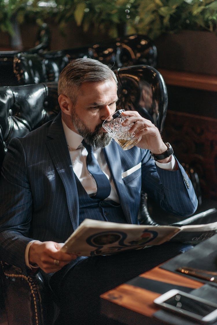 A Man Drinking While Reading The Newspaper 