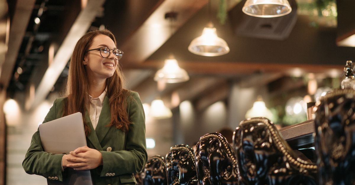 Young person working on laptop in a modern co-working space, smiling confidently