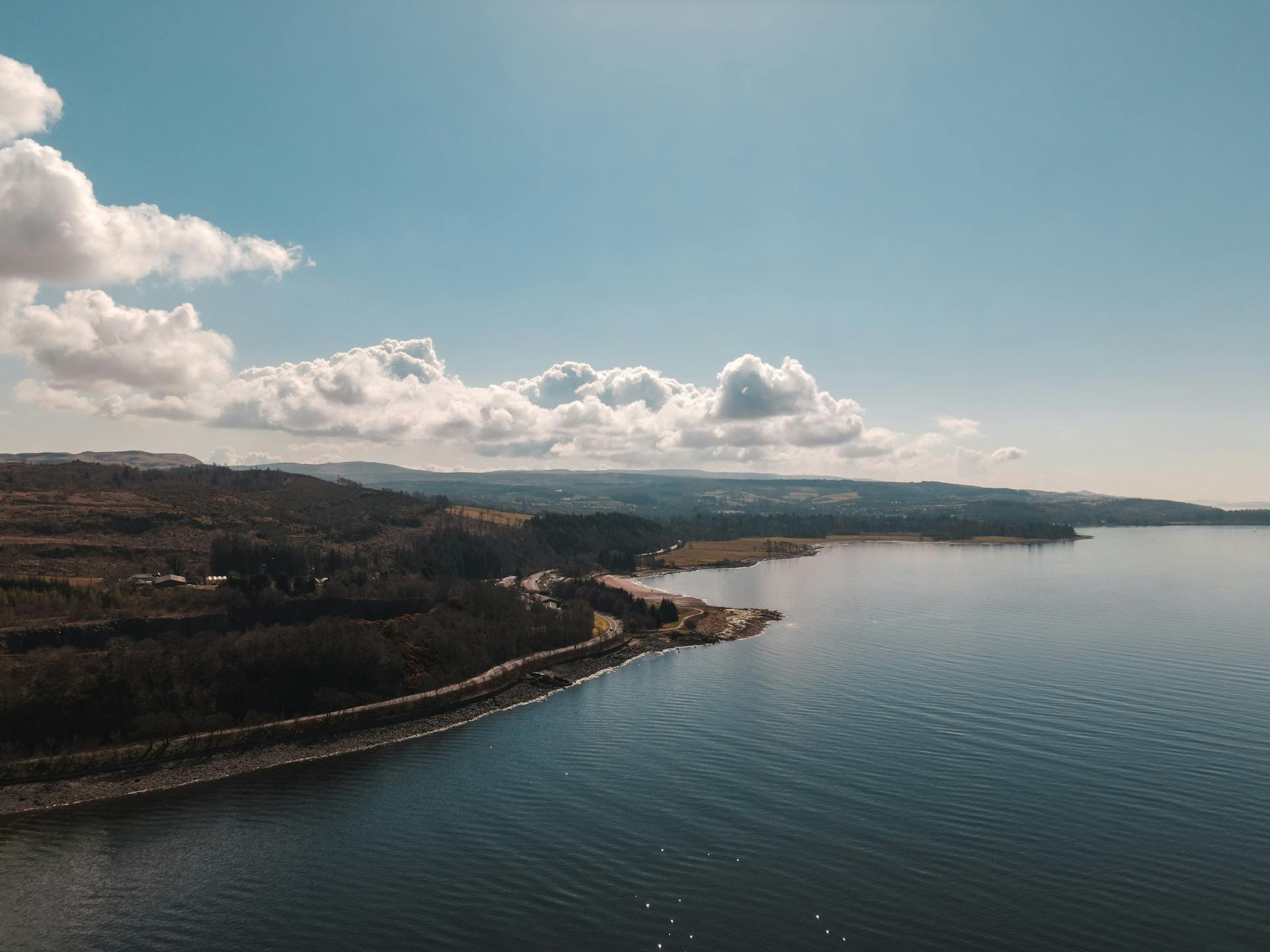Explore the serene beauty of a Scottish loch on a clear day with picturesque clouds.
