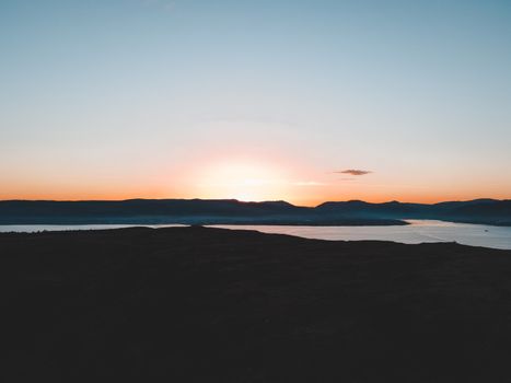 Stunning golden hour view of the Scottish Highlands landscape, capturing the silhouettes of hills against a vibrant sunset.