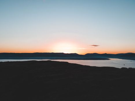 Capture of a stunning sunset over the calm waters and mountains in Scotland, creating a serene atmospheric view.