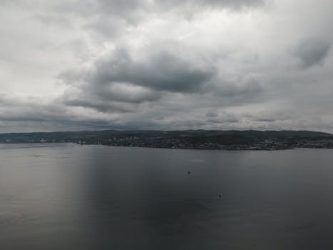 Dramatic aerial view of Greenock, Scotland with cloudy skies over a serene coastline.