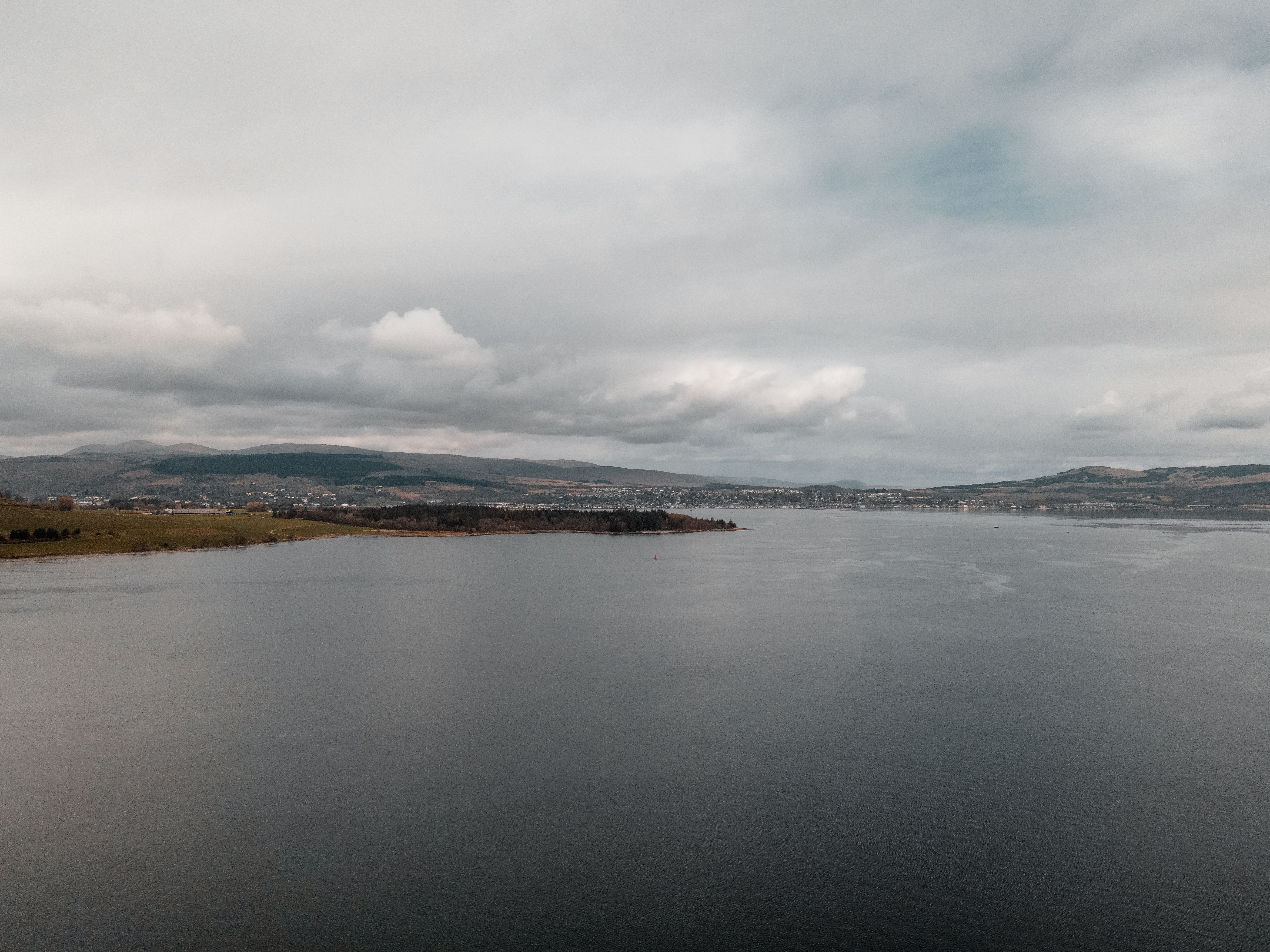 A serene view of Greenock's coastline with calm waters and cloudy sky.