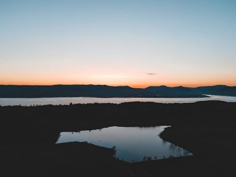 Peaceful sunset over a Scottish lake with reflections and distant mountains.