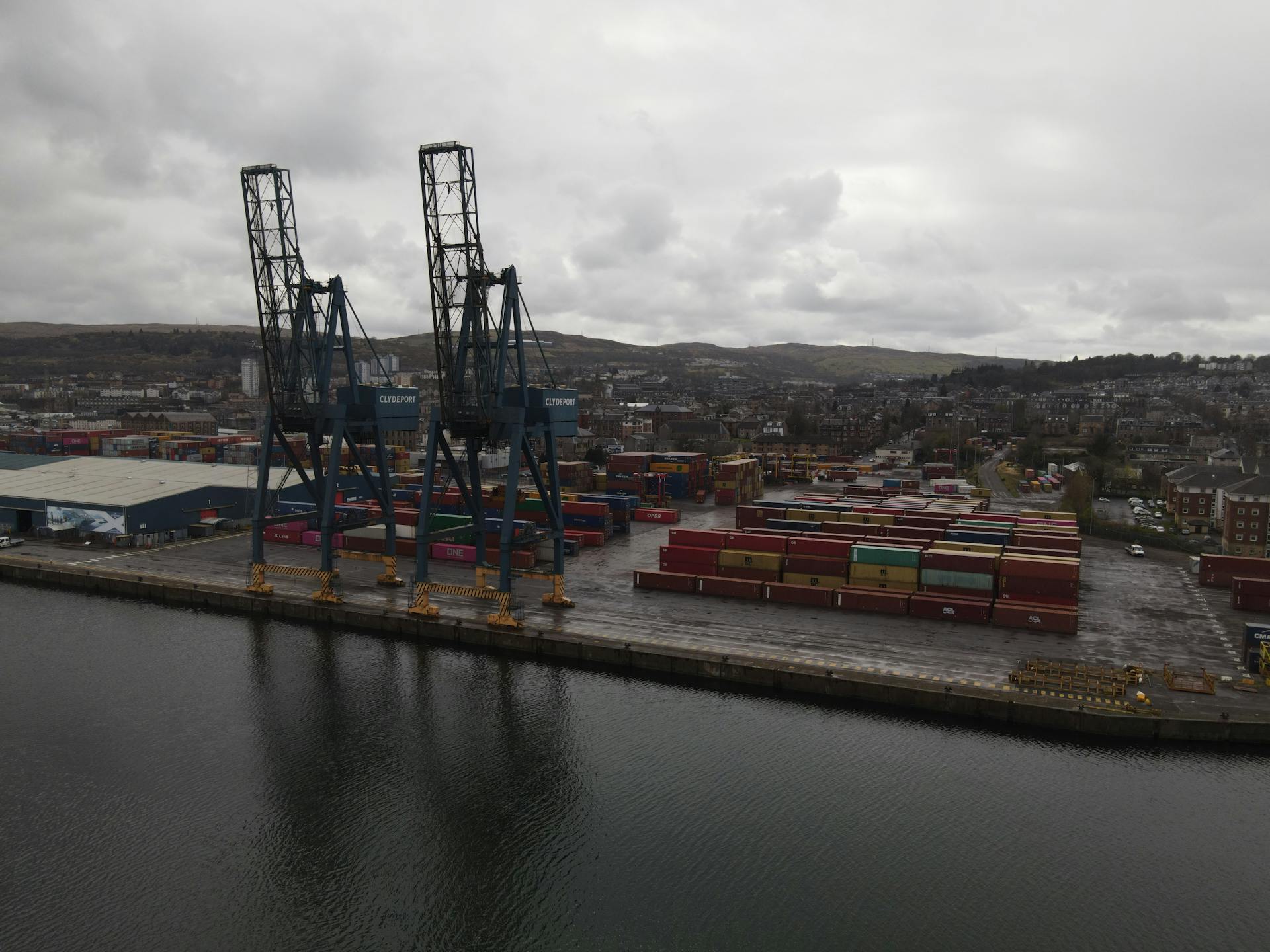 Aerial view of a bustling Scottish port with cranes and cargo containers on a cloudy day.