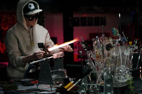 Free Skilled artisan using a blowpipe and flame to create glass art in an indoor workshop setting. Stock Photo