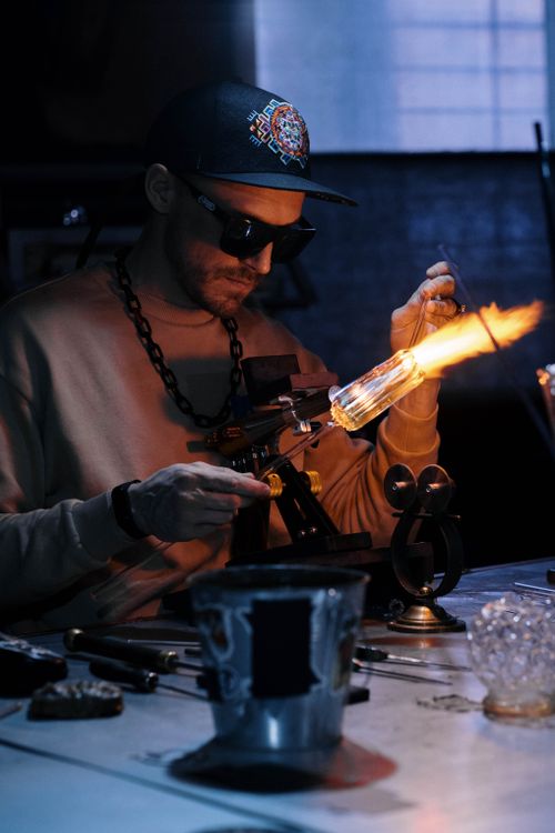 Free Skilled artisan shaping glass with flame in an industrial workshop setting. Stock Photo