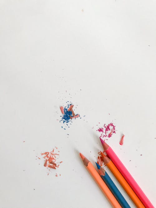 Colorful pencils with shavings on white table