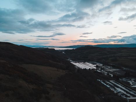 Stunning aerial view of Scotland's lush landscape at twilight, showcasing hills and a serene sunset.