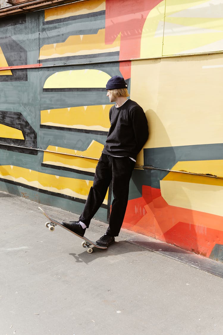 Man Stepping On Skateboard While Leaning On A Wall