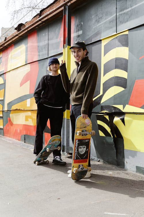 Friends Posing with Their Skateboards in front of a Graffiti Wall