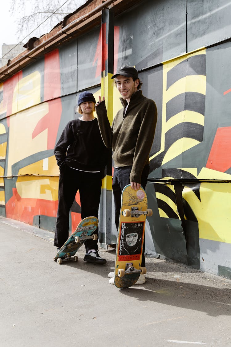 Friends Posing With Their Skateboards In Front Of A Graffiti Wall