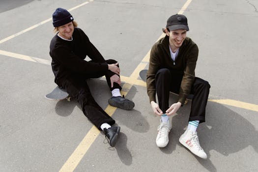 Two young men sitting with skateboards, enjoying a sunny day in casual attire.