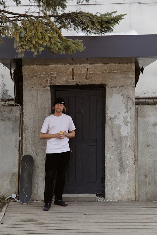 Man in White Crew Neck T-shirt and Black Pants Standing Beside the Black Wooden 