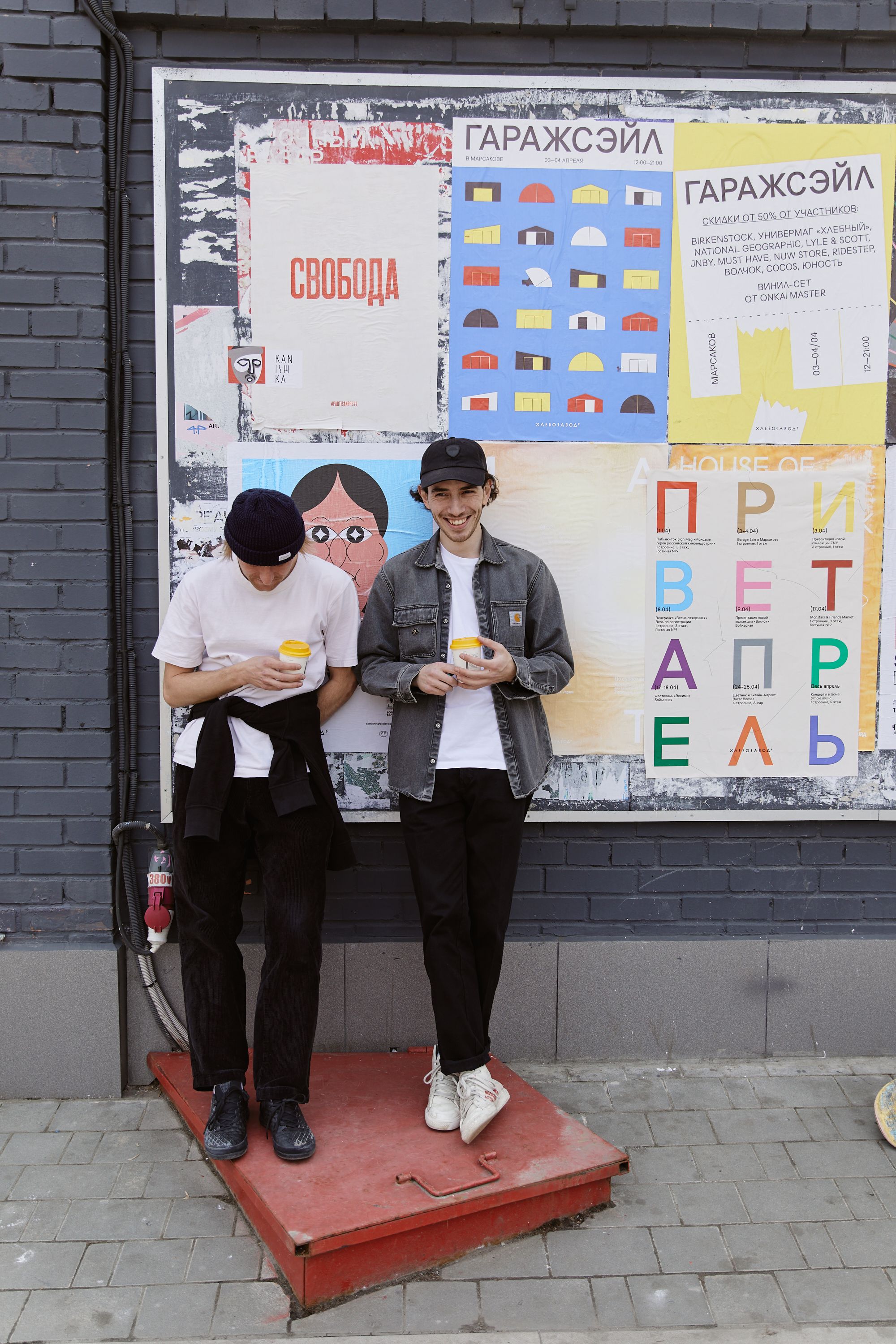 Two young men enjoying beverages and snacks in front of colorful urban posters.