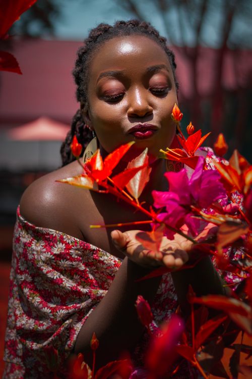 Free Beautiful African woman enjoying vibrant flowers in an outdoor setting. Stock Photo