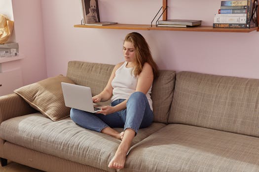 Woman in casual attire using a laptop on a sofa, embodying a relaxing work-from-home setup.