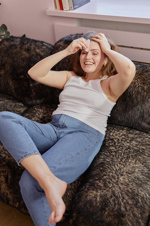A Woman in White Tank Top and Blue Denim Jeans Sitting on a Furry Sofa