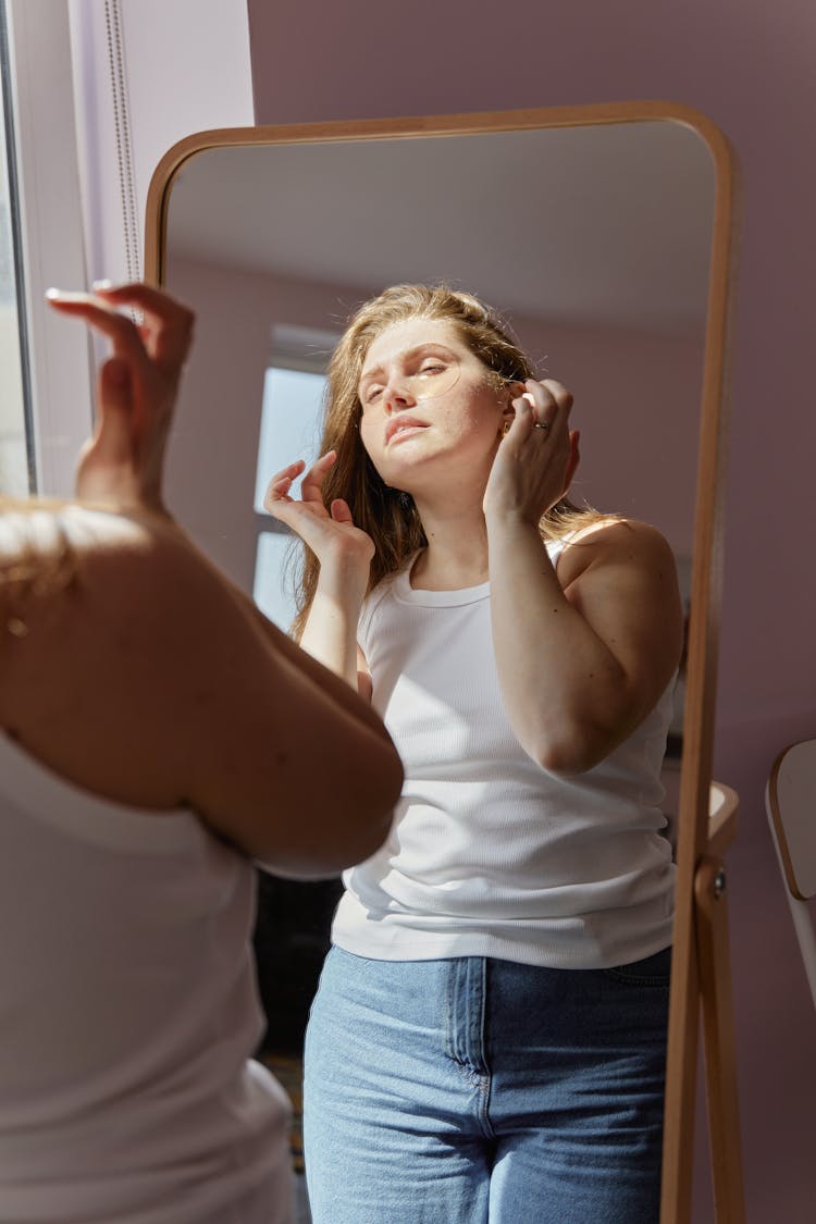 A Woman In White Tank Top Looking At The Mirror