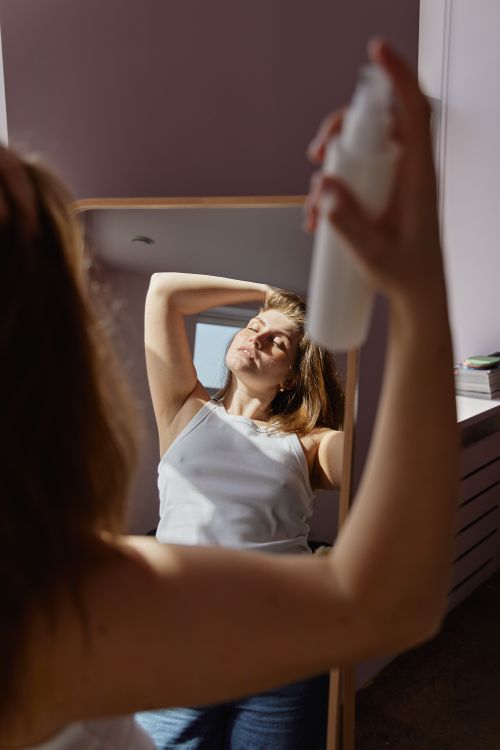Free A woman uses hair spray while looking in a mirror during her beauty routine. Stock Photo