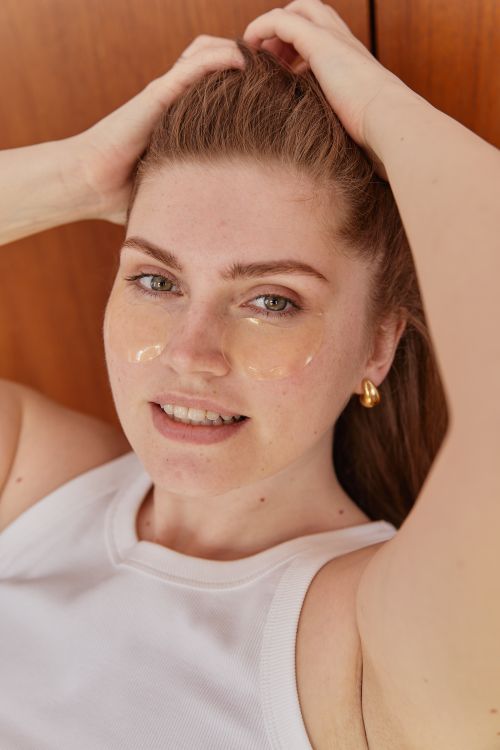 Free A relaxed woman with under eye patches and hands in hair, showcasing a skincare routine indoors. Stock Photo