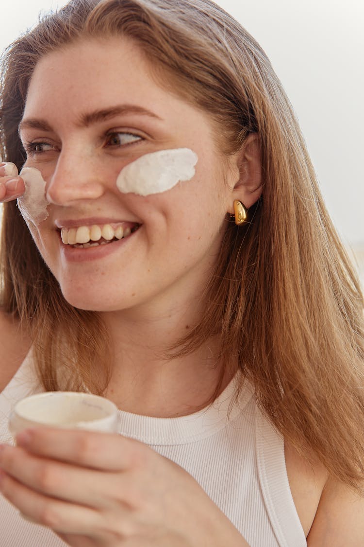 Woman Smiling While Applying Cream On Her Face
