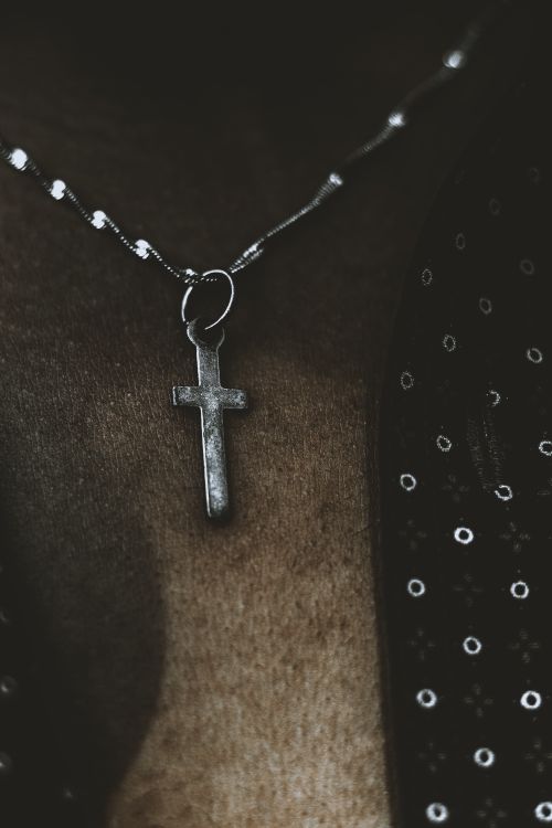 Free A detailed close-up of a silver cross necklace against a textured dark background in vertical shot. Stock Photo