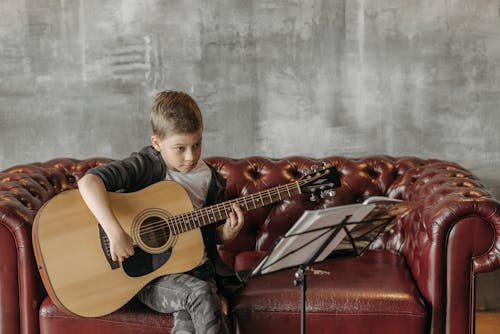 Kid Sitting on a Sofa Playing a Guitar