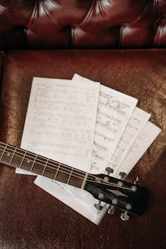 Close-up of a guitar neck on a leather sofa, displaying sheet music.