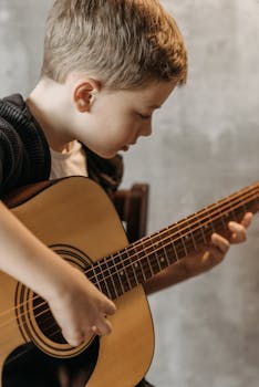 Child practicing guitar chords, focused indoors on musical growth.
