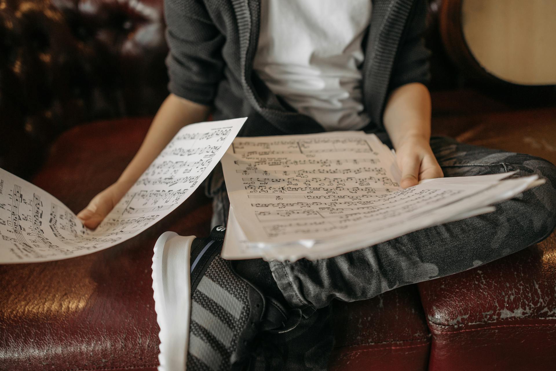 Child sitting on a leather sofa holding sheet music. A close up showcasing musical notation.