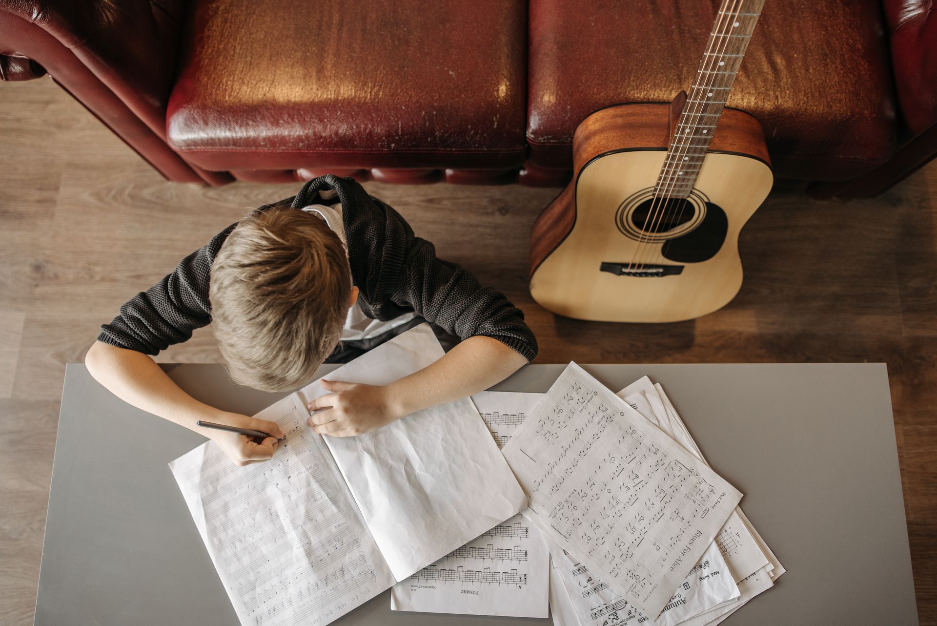 A child writing music notes at home with a guitar on a sofa. Perfect for educational and lifestyle themes.