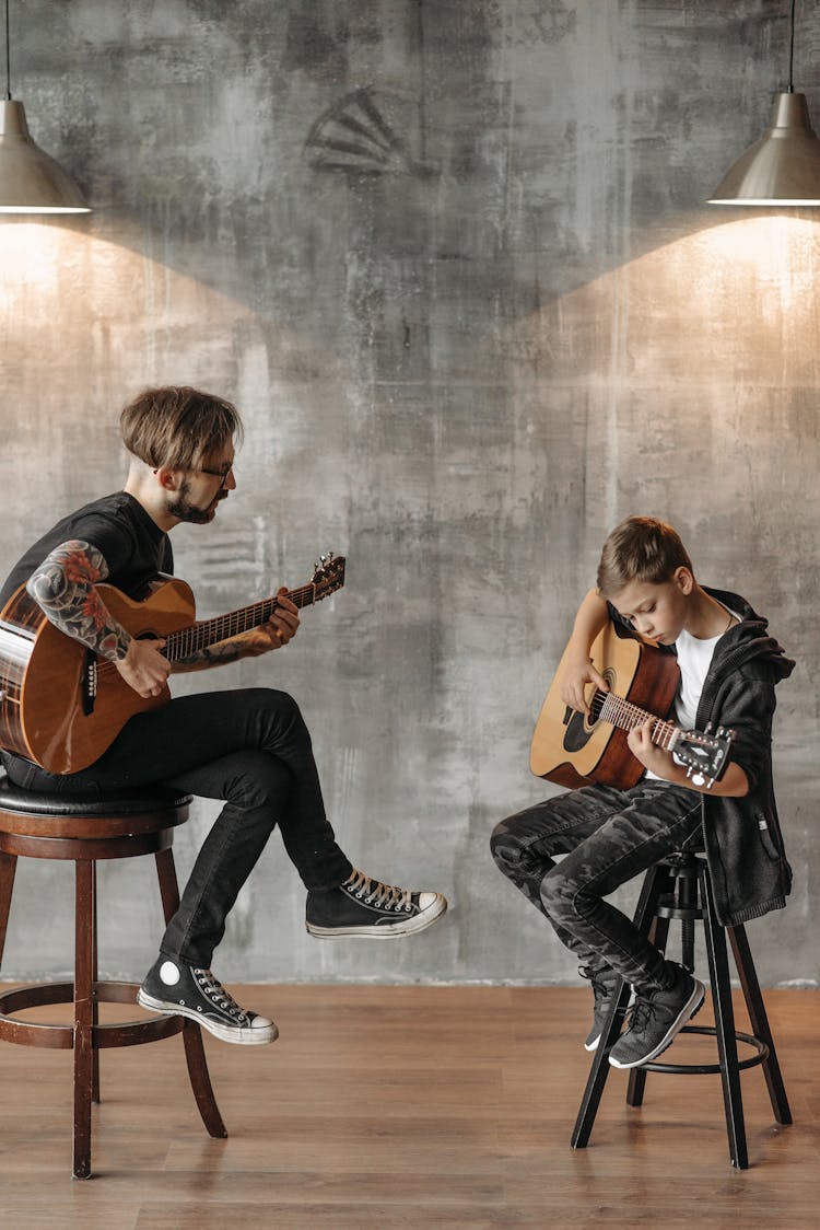 A Tattooed Man And A Young Boy Playing Guitar Together