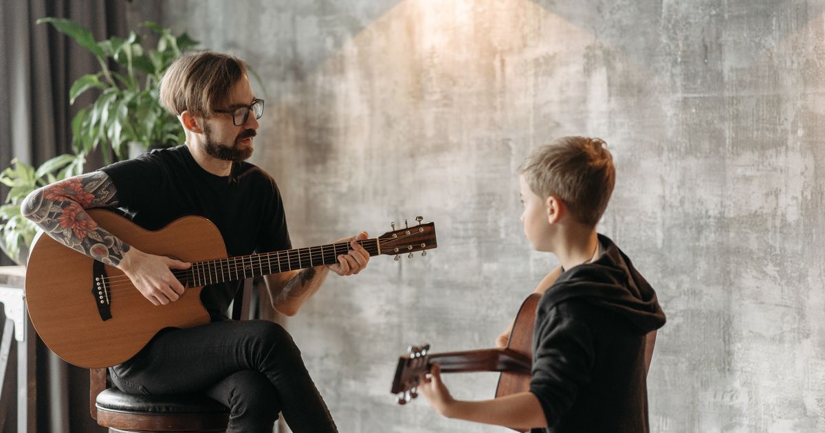 A guitarist teaching a student in a home studio, surrounded by musical instruments.