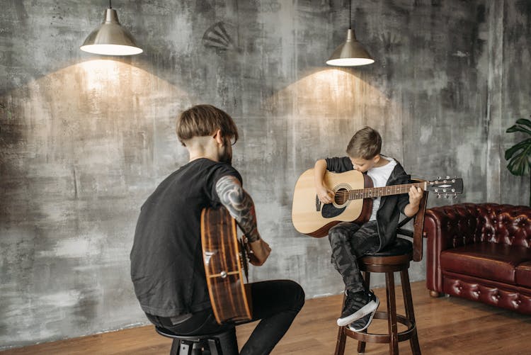 A Man Teaching A Boy How To Play The Guitar