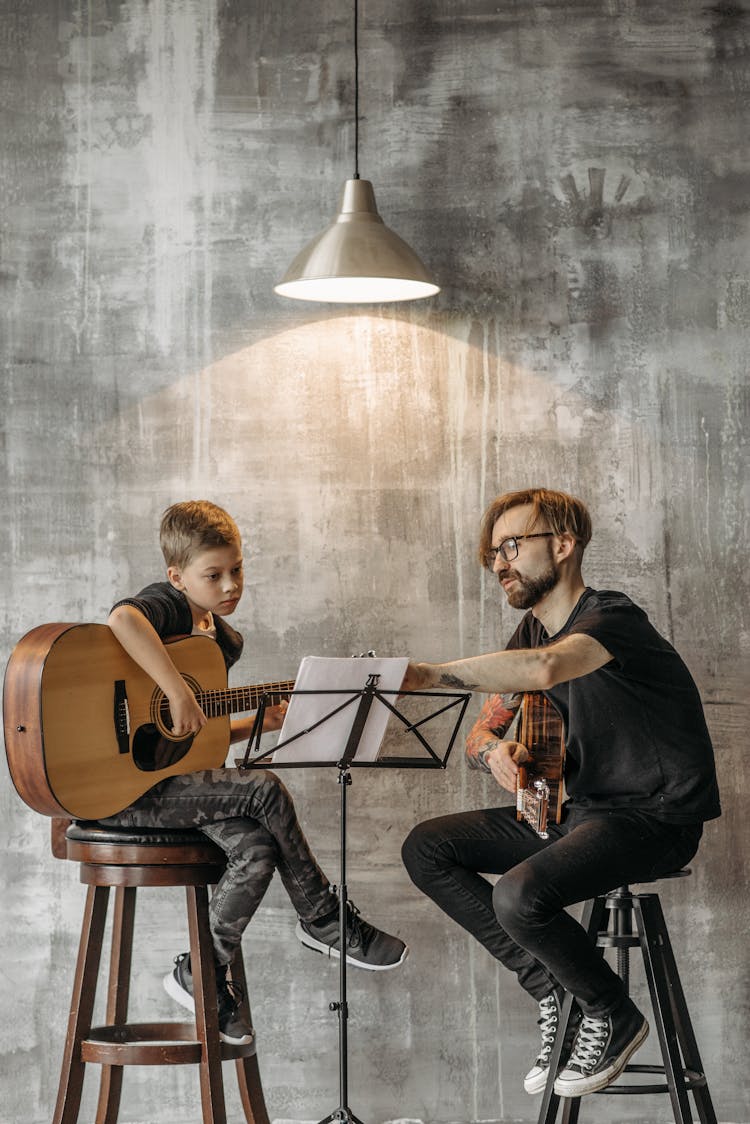 A Man Teaching A Boy How To Play The Guitar